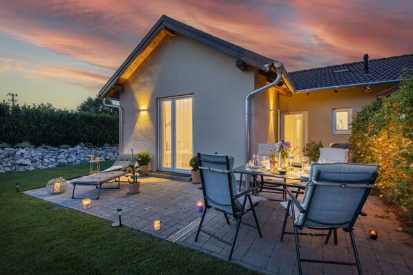 A house with a patio, outdoor seating, and a well-lit entrance.