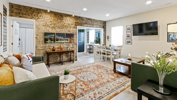 A spacious living room with a brick wall, a dining area, and a TV mounted on the wall.