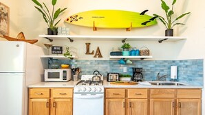 A kitchen with wooden cabinets, a white stove, a microwave, and a surfboard on the wall.