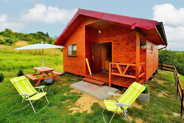 A wooden cabin with a porch, a picnic table, and two lawn chairs.