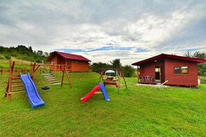 A grassy outdoor area with two wooden cabins, a playground with slides, and a swing set. - Summer House in Rusinowo near Seaside Beach (Jaroslawiec)