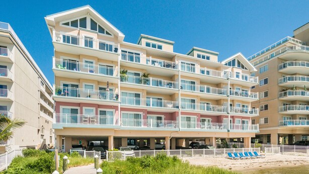 Un hotel de varios pisos con balcones, zona de estacionamiento y vista al mar.