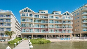 Un hotel de varios pisos con balcones, un paseo marítimo que conduce a la playa y una vista despejada del agua.