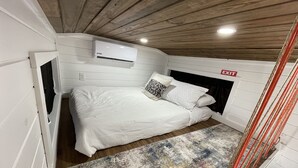 Um quarto pequeno e acolhedor com uma cama, um tapete colorido e teto de madeira.