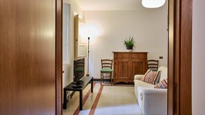 Una sala de estar con un sofá, televisión, aparador y una planta.