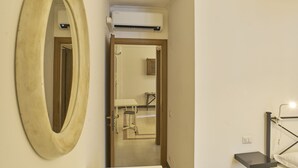 Una habitación con un espejo ovalado grande, una cama con estructura metálica negra y un equipo de aire acondicionado blanco montado sobre una puerta.