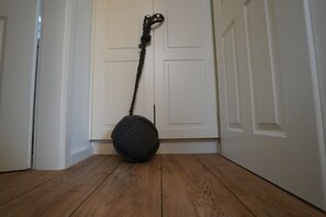Un suelo de madera y un objeto redondo oscuro con asa de cuerda frente a una puerta blanca.