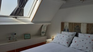Un dormitorio con techo inclinado, una cama con ropa de cama blanca, una mesita de noche, una decoración con tabla de surf y un panel de madera en la pared.