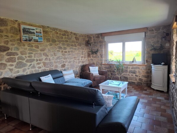 A stone-walled room with a black leather sofa, a brown leather armchair, and a white cabinet.