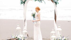 Decoración para una boda en la playa, con un arco blanco, arreglos florales y faroles.