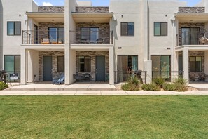 A modern multi-story residential building with balconies, outdoor seating, and a well-maintained lawn. - Red Rock Oasis: Desert Color Lagoon + Beaches (St. George)