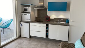 A modern kitchen with white cabinets, a stainless steel range hood, a microwave, and a dishwasher. There is a blue wall-mounted cabinet above the sink and a small red appliance on the counter. - Apartment T2 air-conditioned - Beach - Downtown (Saintes-Maries-de-la-Mer)