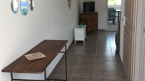 A hallway with a wooden table, a TV on a cabinet, and a door leading to an outdoor area. - Apartment T2 air-conditioned - Beach - Downtown (Saintes-Maries-de-la-Mer)