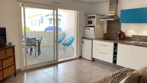 A modern kitchen with a microwave, oven, and red appliance, a dining area with chairs, and a sliding glass door leading to an outdoor seating area. - Apartment T2 air-conditioned - Beach - Downtown (Saintes-Maries-de-la-Mer)