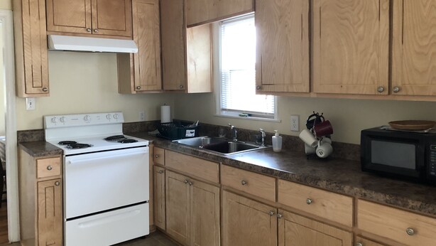 A kitchen with wooden cabinets, a white stove, a sink, and a microwave. - Lovely 3bdrm home walking distance from Masters (Augusta)