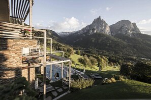 A mountain lodge with a pool area, outdoor seating, and a view of the surrounding mountains.