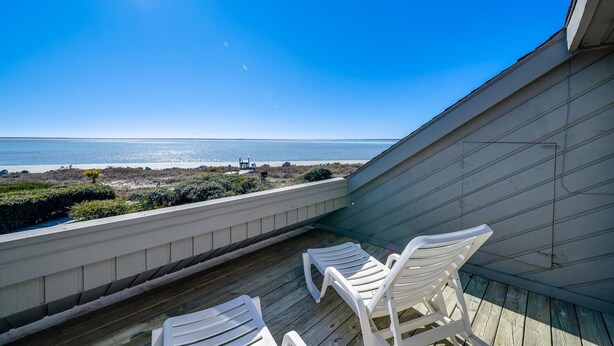 Un balcon avec deux chaises blanches donnant sur une plage.