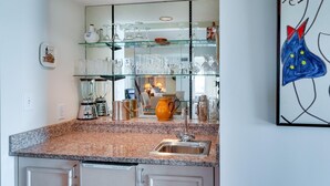 Une cuisine dotée de plans de travail en granit, d’un évier en acier inoxydable et d’étagères en verre au-dessus, où sont rangés divers ustensiles de cuisine.