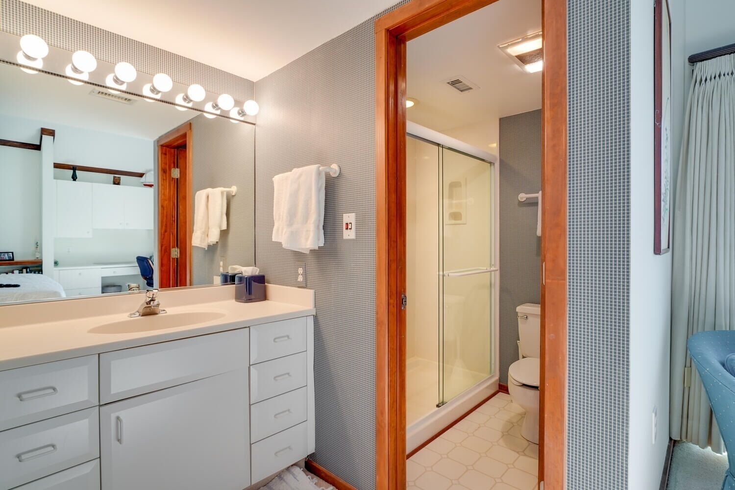 A modern bathroom with a large mirror, vanity, and a glass-enclosed shower.