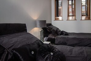 Quarto de hotel com duas camas, uma mesinha de cabeceira, um abajur e janela com vista para o exterior.