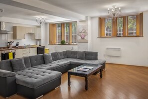 Uma sala de estar moderna com um sofá seccional, uma mesa de centro de vidro e uma cozinha com armários de madeira e fogão.