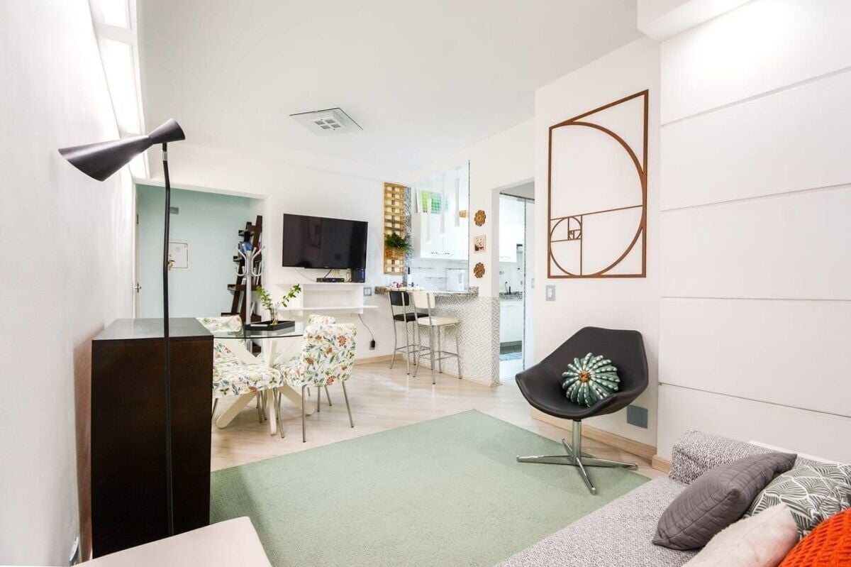A modern living room with a sofa, a coffee table, and a TV. There is a dining area with a table and chairs.
