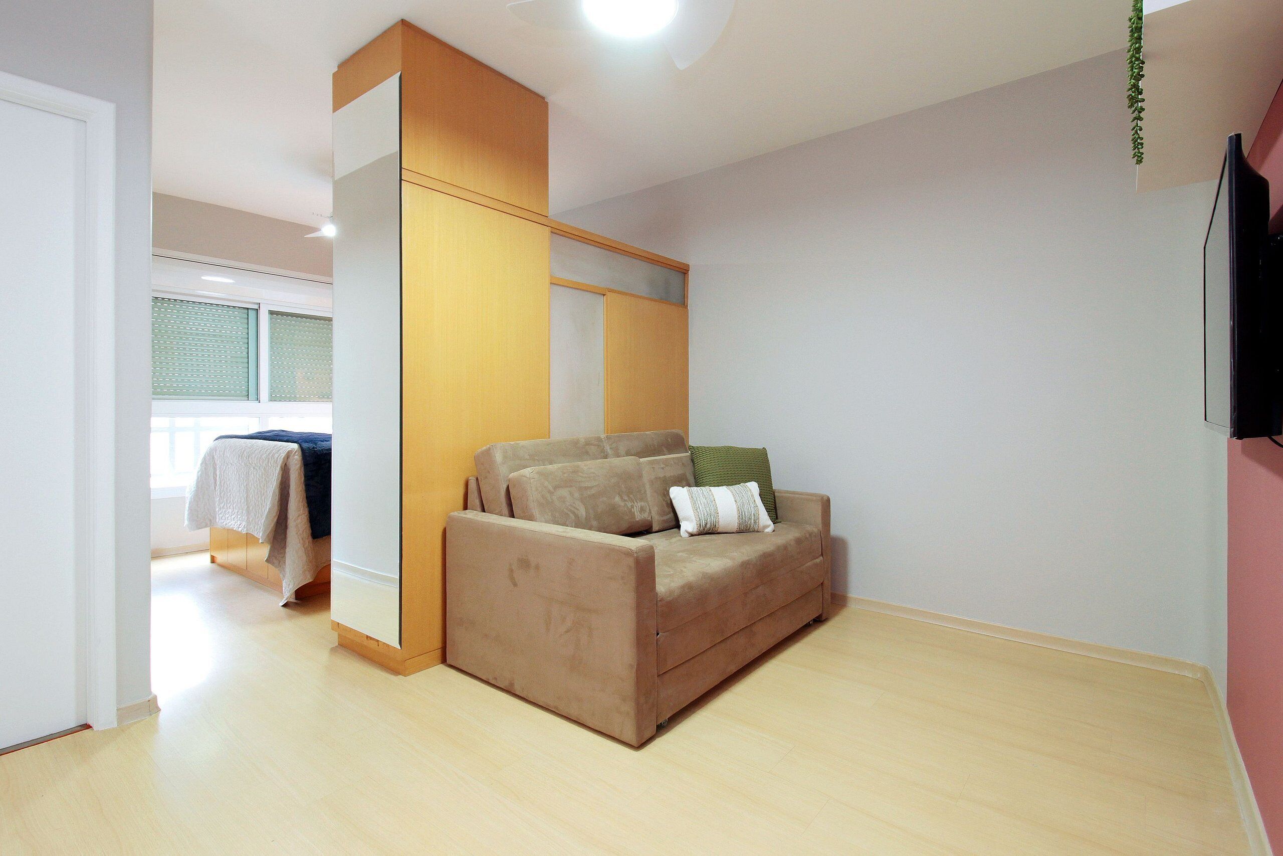 Um quarto com um sofá bege, um guarda-roupa de madeira e uma cama com colcha branca.