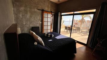 Ein Schlafzimmer mit einem großen Bett, einer Glasschiebetür, die zu einer Außenpatio mit Stühlen und einem Tisch führt.