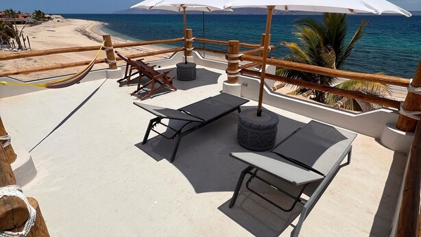 Een terras aan het strand met lounge fauteuils, een tafel en parasols, met uitzicht op de oceaan.