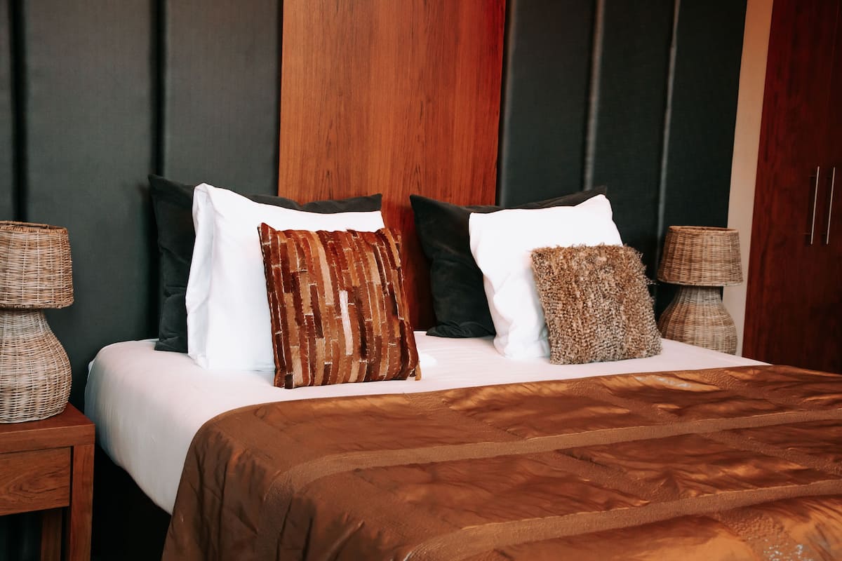 Ein Bett mit brauner Bettdecke, zwei Nachttische mit Lampen und ein dunkles Holz-Kopfbrett.