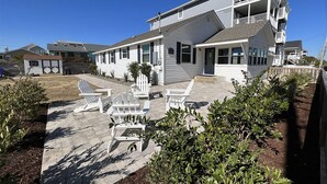 Een huis met twee verdiepingen, een balkon, een overdekte patio met Adirondack-stoelen en een kleine schuur in de achtertuin.
