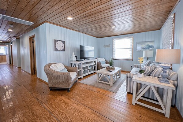 A spacious living room with a wooden ceiling, a television, wicker furniture, and a striped sofa.
