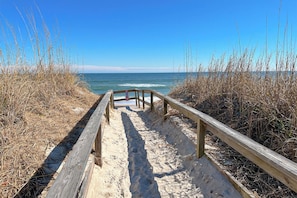 A wooden boardwalk leading to the beach, surrounded by dry grass and sand.
