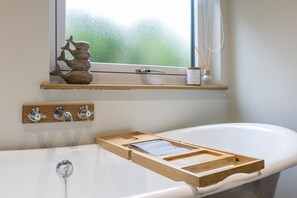 A bathroom with a bathtub, wooden shelf with decorative items, and a window with a view.