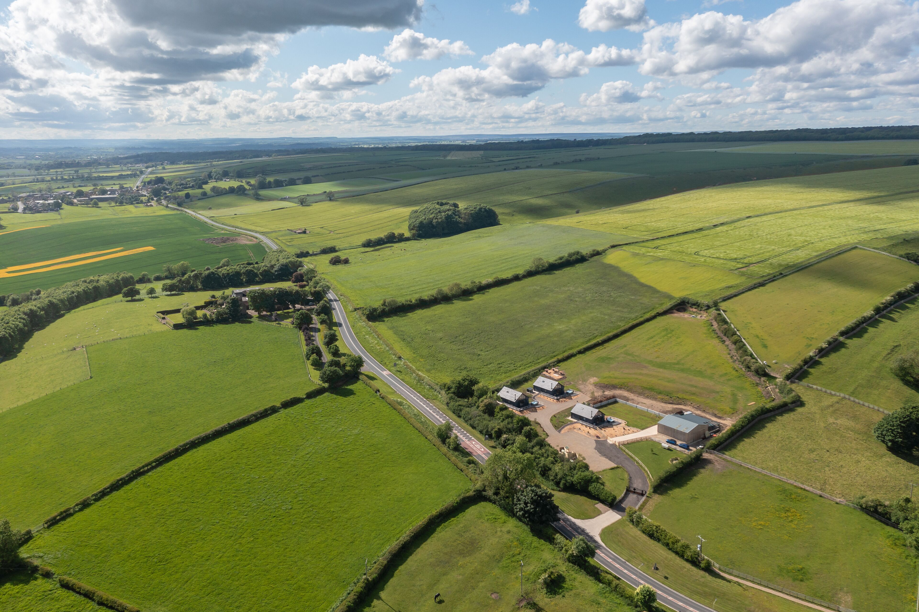 An aerial view of a rural landscape with fields, a winding road, and a small cluster of buildings.