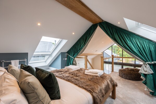 A bedroom with a sloped ceiling, a large bed, a window, and a view of the outdoors.