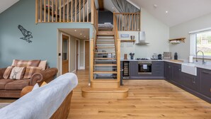 A spacious living area with a wooden staircase leading to an upper level, a kitchen with modern appliances, and a cozy seating area with a sofa and cushions. - Eagles Peak (Pickering)