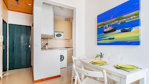 A compact kitchen with a washing machine, a microwave, and a dining area with a table set for two. - 1BR Apartment - Downtown Lisbon - Chiado (Lisbon)
