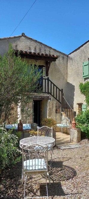 A stone building with a staircase, outdoor seating, and a metal table and chair. - Whole cozy country cottage in South of France. (Frausseilles)