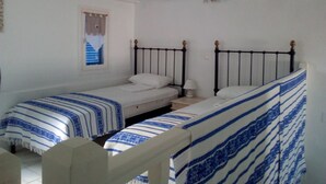 Een kamer met twee eenpersoonsbedden, een raam met gordijnen en een wit plafond met zichtbare balken.