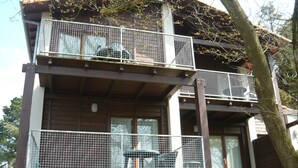Un bâtiment en bois à deux étages, doté de balcons, d’un espace extérieur couvert et d’un arbre au premier plan.