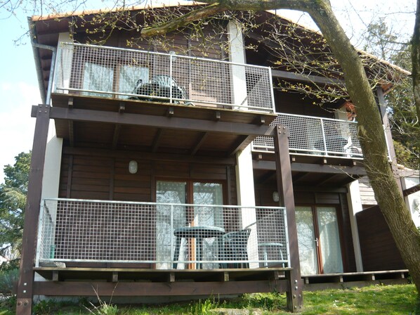 A two-story wooden building with balconies, a covered outdoor area, and a tree in the foreground.
