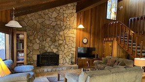 A cozy living room with a stone fireplace, a television, and a staircase. - RR18 National Forest Views! (Black Butte Ranch)