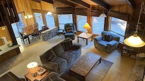 A spacious living area with a large sofa, a coffee table, and a dining table with chairs. There are large windows providing a view of the outdoors. - RR18 National Forest Views! (Black Butte Ranch)