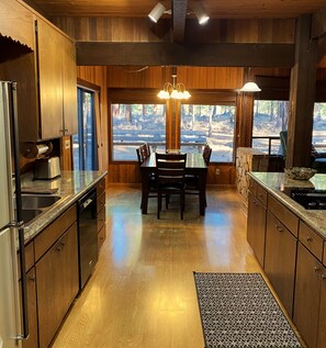 A modern kitchen with wooden cabinets, a dining table, and large windows offering a view of the outdoors. - RR18 National Forest Views! (Black Butte Ranch)