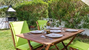 Un espace de restauration en plein air avec une table en bois prévue pour quatre personnes, entourée de chaises confortables aux coussins verts.