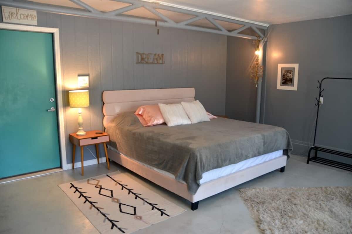 Una camera da letto con un letto, lampade sui comodini, un tappeto, una porta e un cartello appeso al muro.
