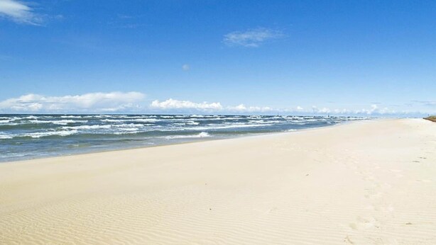 A sandy beach with waves and a clear sky.