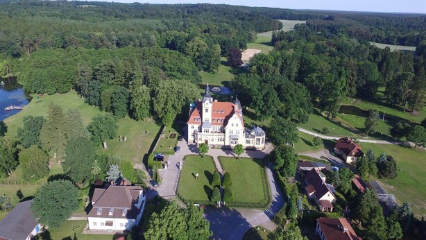 An aerial view of a large estate with a central building surrounded by lush greenery and a lake.