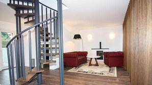 A modern living room with a spiral staircase, red sofas, a round coffee table, and a fireplace.